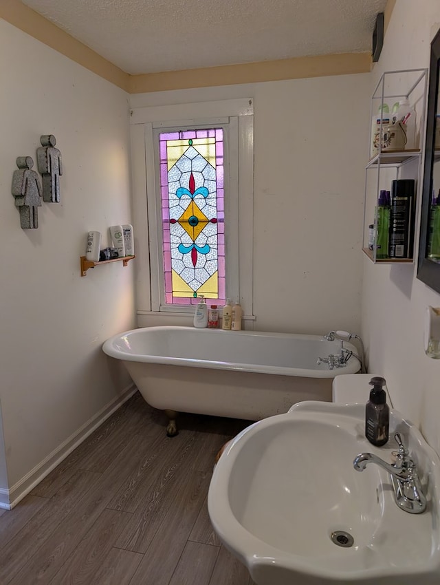 full bathroom with a textured ceiling, a sink, wood finished floors, baseboards, and a freestanding bath