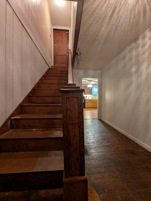 staircase with a textured ceiling, baseboards, and wood finished floors