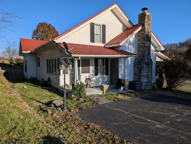 view of front of house featuring metal roof, covered porch, a front lawn, a chimney, and a patio area