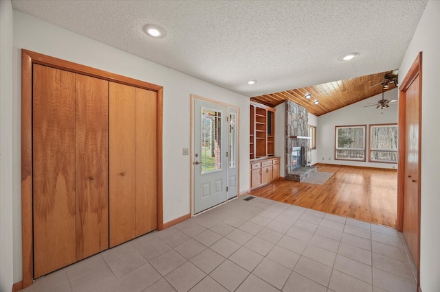 foyer with light tile patterned floors, a fireplace, a textured ceiling, and vaulted ceiling