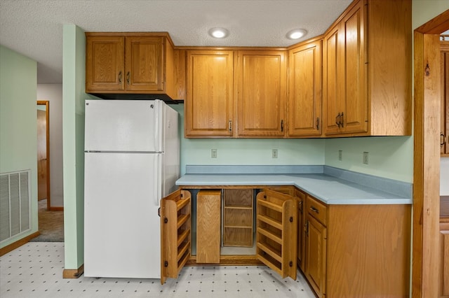 kitchen featuring light countertops, visible vents, freestanding refrigerator, and brown cabinets