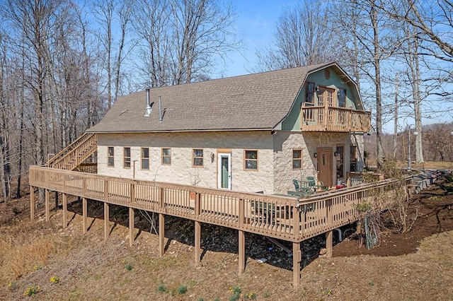 back of property featuring a balcony, a deck, a gambrel roof, and roof with shingles