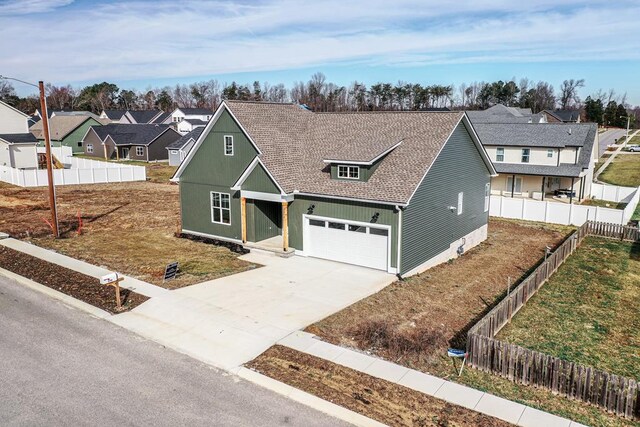 traditional-style home featuring driveway, a garage, a residential view, roof with shingles, and fence