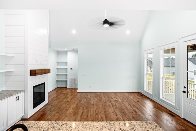 unfurnished living room featuring dark wood-type flooring, a glass covered fireplace, vaulted ceiling, ceiling fan, and baseboards