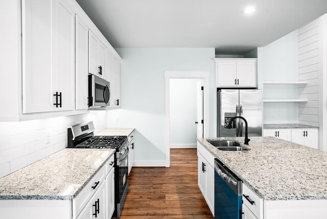 kitchen with open shelves, appliances with stainless steel finishes, white cabinets, a sink, and light stone countertops