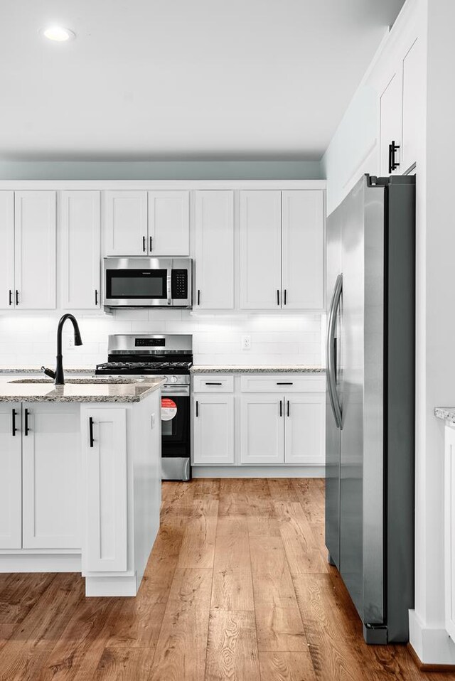 kitchen with light stone counters, backsplash, appliances with stainless steel finishes, white cabinets, and a sink