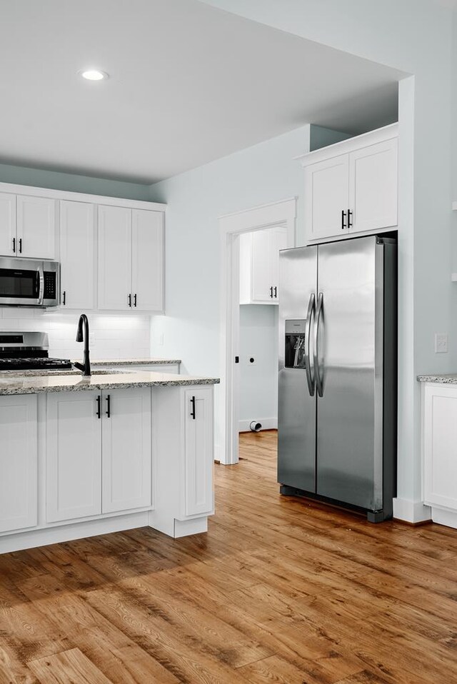 kitchen featuring light stone countertops, light wood-style flooring, appliances with stainless steel finishes, and white cabinets