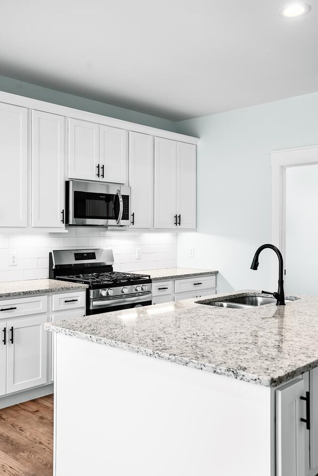 kitchen with white cabinets, an island with sink, light stone counters, stainless steel appliances, and a sink