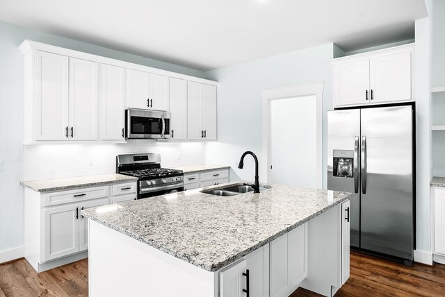 kitchen with a center island with sink, appliances with stainless steel finishes, light stone countertops, white cabinetry, and a sink