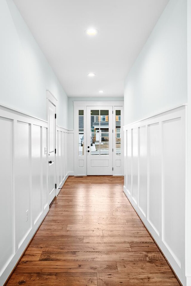 hallway with wainscoting, light wood-style flooring, a decorative wall, and recessed lighting