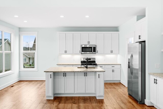 kitchen with appliances with stainless steel finishes, white cabinetry, an island with sink, and light stone countertops