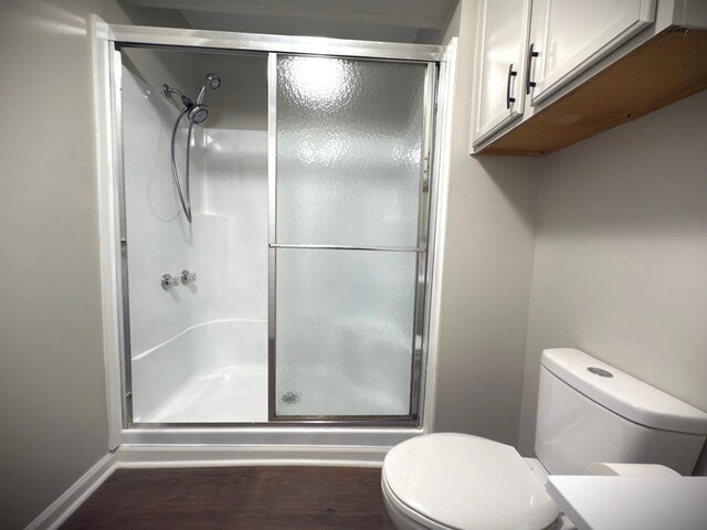 bathroom featuring a stall shower, baseboards, toilet, and wood finished floors