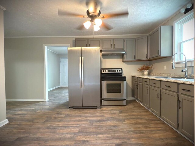 kitchen with dark wood finished floors, appliances with stainless steel finishes, ornamental molding, under cabinet range hood, and a sink