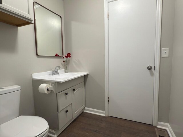 half bath featuring toilet, wood finished floors, visible vents, vanity, and baseboards