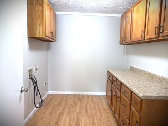 laundry room with cabinet space, baseboards, a textured ceiling, light wood-type flooring, and washer hookup