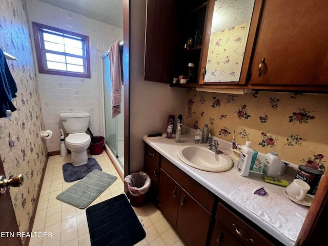 bathroom with toilet, vanity, tile patterned floors, a stall shower, and wallpapered walls