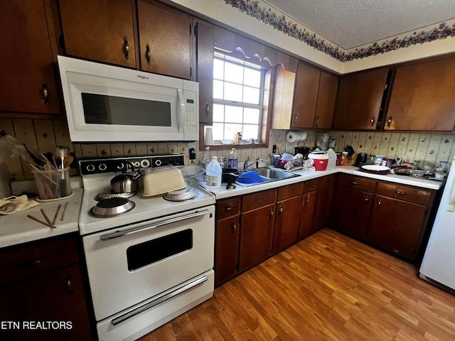 kitchen with light wood-type flooring, white appliances, light countertops, and a textured ceiling