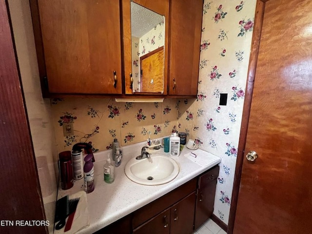 bathroom featuring baseboards, vanity, and wallpapered walls