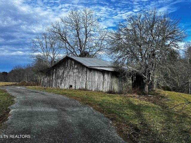 view of property exterior with aphalt driveway, an outbuilding, and metal roof