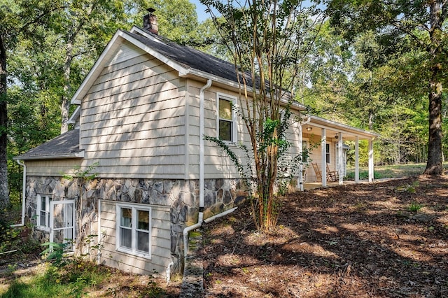 view of side of home with a shingled roof, stone siding, and a chimney