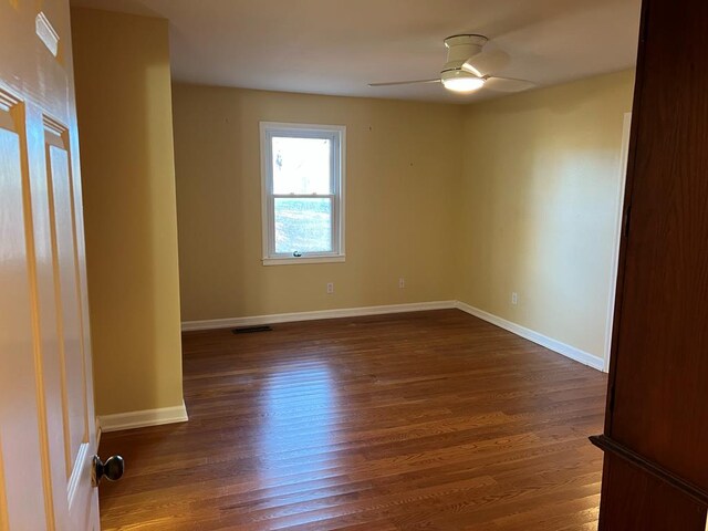 spare room with a ceiling fan, dark wood-style flooring, visible vents, and baseboards