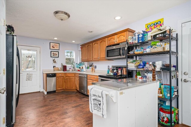 kitchen featuring appliances with stainless steel finishes, brown cabinets, dark wood-type flooring, a peninsula, and a sink