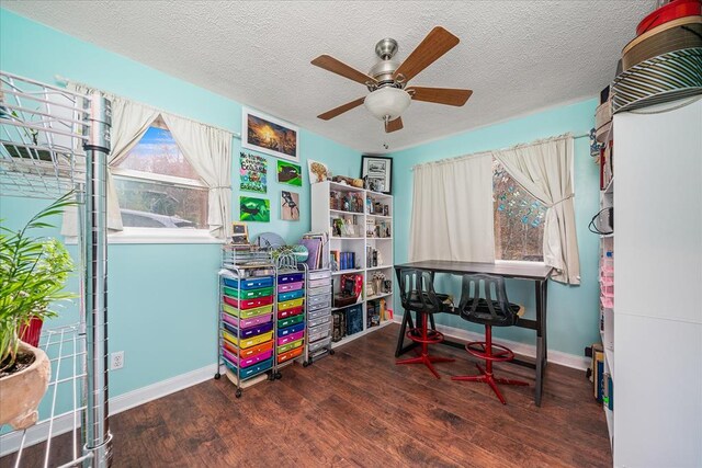 recreation room with a ceiling fan, a textured ceiling, baseboards, and dark wood-style flooring