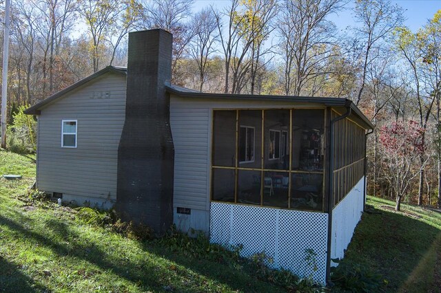 view of side of property featuring crawl space, a sunroom, a chimney, and a lawn