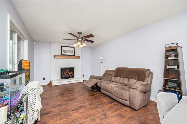 living area featuring dark wood-type flooring, a brick fireplace, ceiling fan, and baseboards