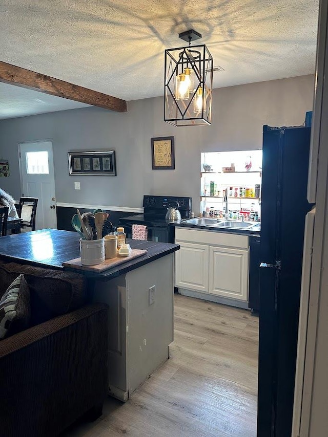 kitchen featuring a textured ceiling, a sink, white cabinetry, light wood-style floors, and pendant lighting