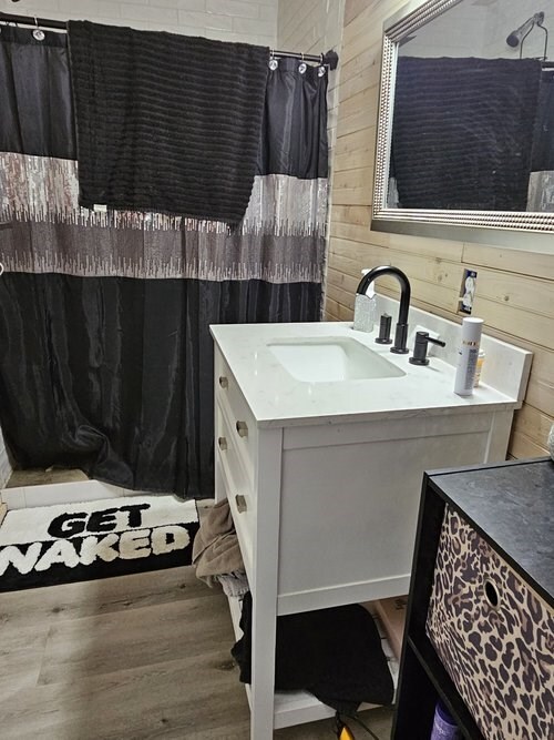 full bath featuring a shower with curtain, wooden walls, wood finished floors, and vanity