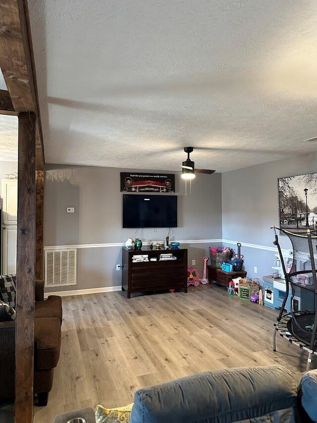 living area featuring visible vents, a ceiling fan, a textured ceiling, light wood-type flooring, and baseboards