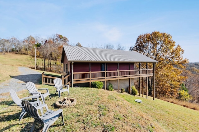 rear view of house featuring a deck, an outdoor fire pit, a yard, and metal roof