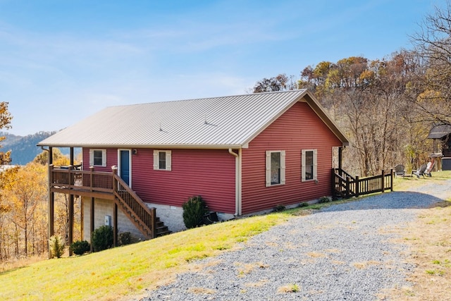 back of house featuring a deck, driveway, a yard, stairway, and metal roof