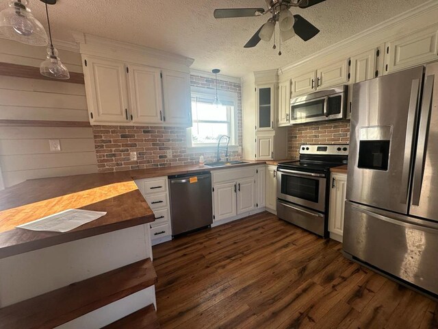 kitchen featuring white cabinets, dark wood finished floors, stainless steel appliances, pendant lighting, and a sink