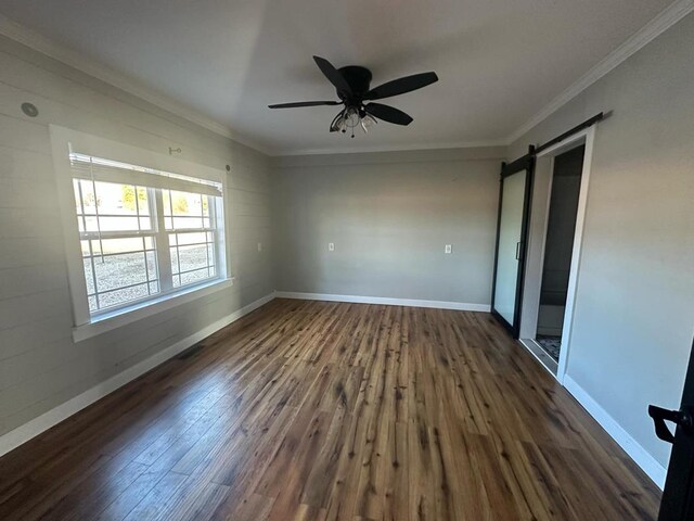 empty room featuring ornamental molding, baseboards, dark wood-style floors, and a barn door