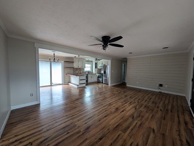 unfurnished living room featuring dark wood-style floors, ornamental molding, and ceiling fan with notable chandelier