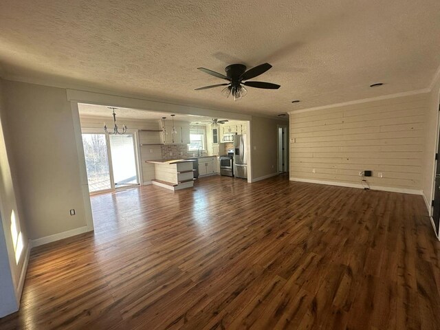 unfurnished living room featuring ceiling fan with notable chandelier, a sink, dark wood finished floors, and baseboards