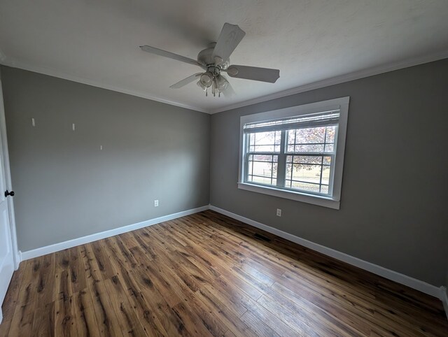 spare room featuring crown molding, baseboards, ceiling fan, and dark wood-style flooring