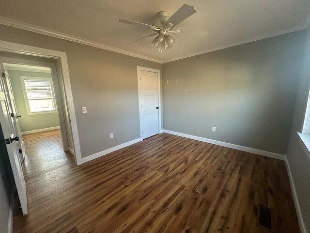 unfurnished bedroom featuring ceiling fan, visible vents, baseboards, dark wood-style floors, and crown molding