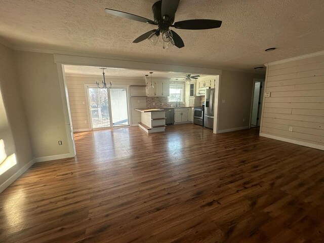 unfurnished living room with a textured ceiling, baseboards, dark wood-style flooring, and ceiling fan with notable chandelier