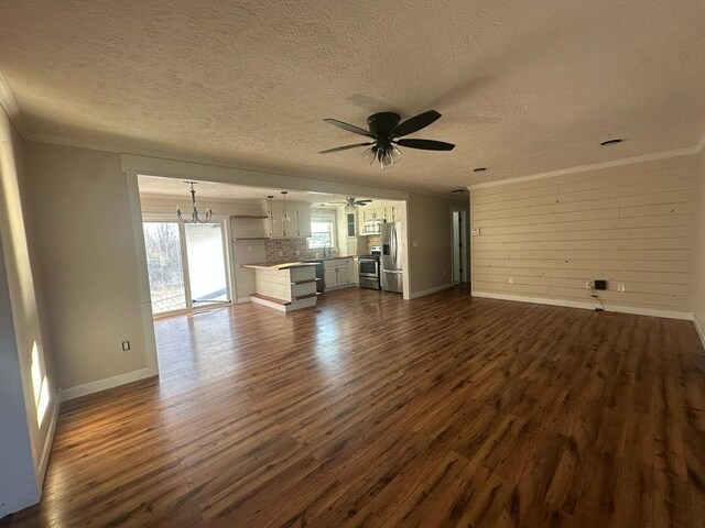 unfurnished living room featuring crown molding, dark wood-type flooring, a textured ceiling, baseboards, and ceiling fan with notable chandelier