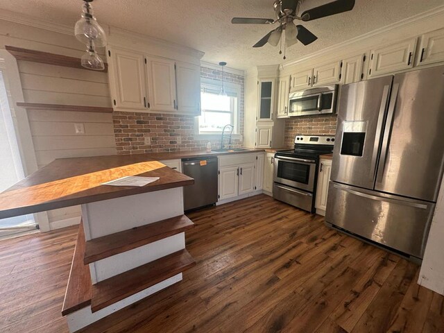 kitchen featuring pendant lighting, dark wood-style flooring, stainless steel appliances, white cabinetry, and a sink