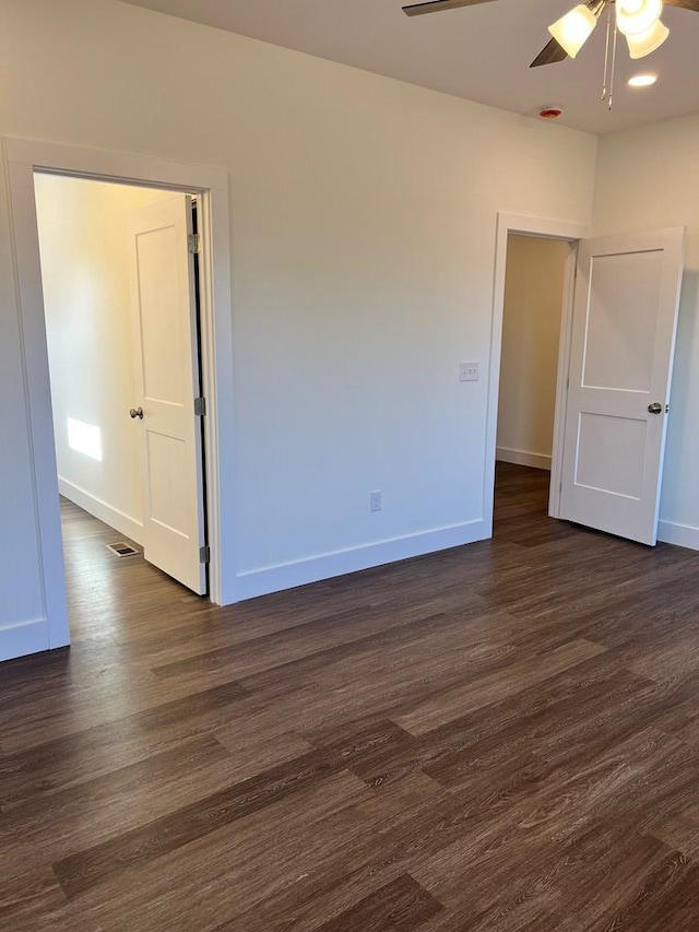 empty room featuring ceiling fan, dark wood-type flooring, visible vents, and baseboards