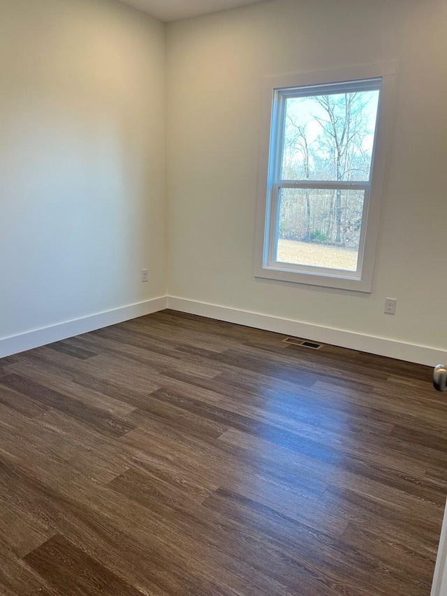 spare room featuring dark wood-type flooring, visible vents, and baseboards