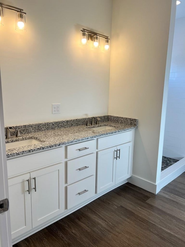 full bathroom with wood finished floors, a sink, baseboards, and double vanity