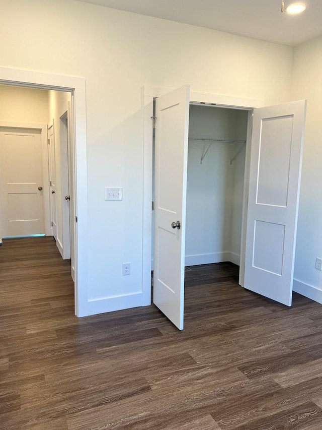 unfurnished bedroom with dark wood-type flooring, a closet, and baseboards