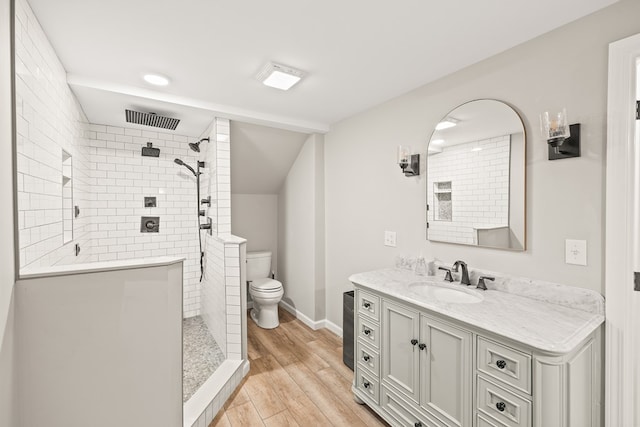 bathroom featuring toilet, wood finished floors, visible vents, vanity, and a tile shower