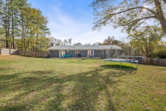 back of house featuring a yard, a trampoline, and a fenced backyard