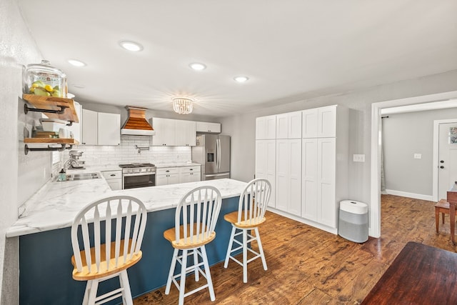 kitchen with white cabinets, appliances with stainless steel finishes, a breakfast bar area, custom exhaust hood, and a sink